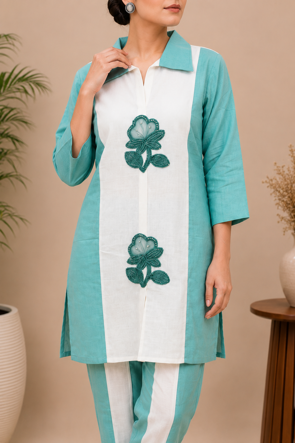 A woman modeling a two-piece kurta and trouser set in mint green and white, featuring a vertical white stripe on the kurta with two green floral prints, set against a warm beige background with decorative plants.