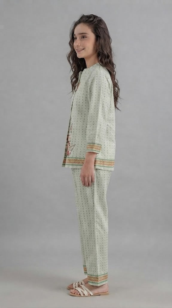 A woman modeling a light sage green two-piece kurta set with a small geometric pattern, featuring colorful embroidered details on the chest and sleeve cuffs, paired with matching wide-leg trousers.
