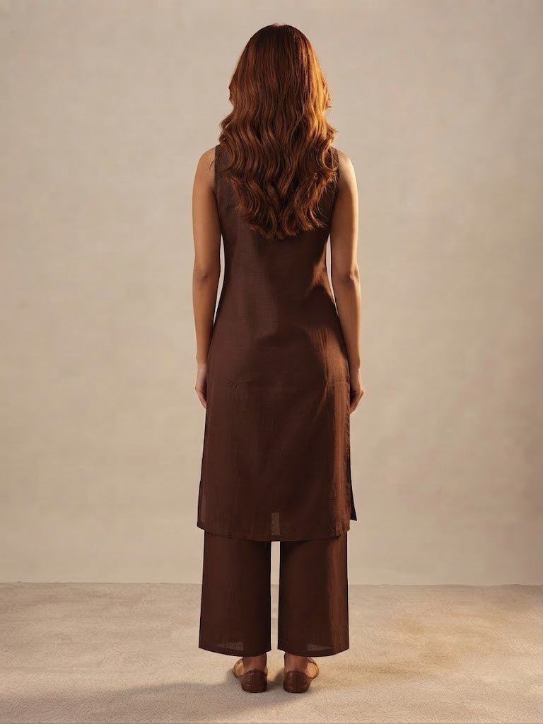 A woman modeling a dark brown sleeveless kurta with floral and butterfly embroidery, paired with matching wide-leg trousers, in a studio setting.
