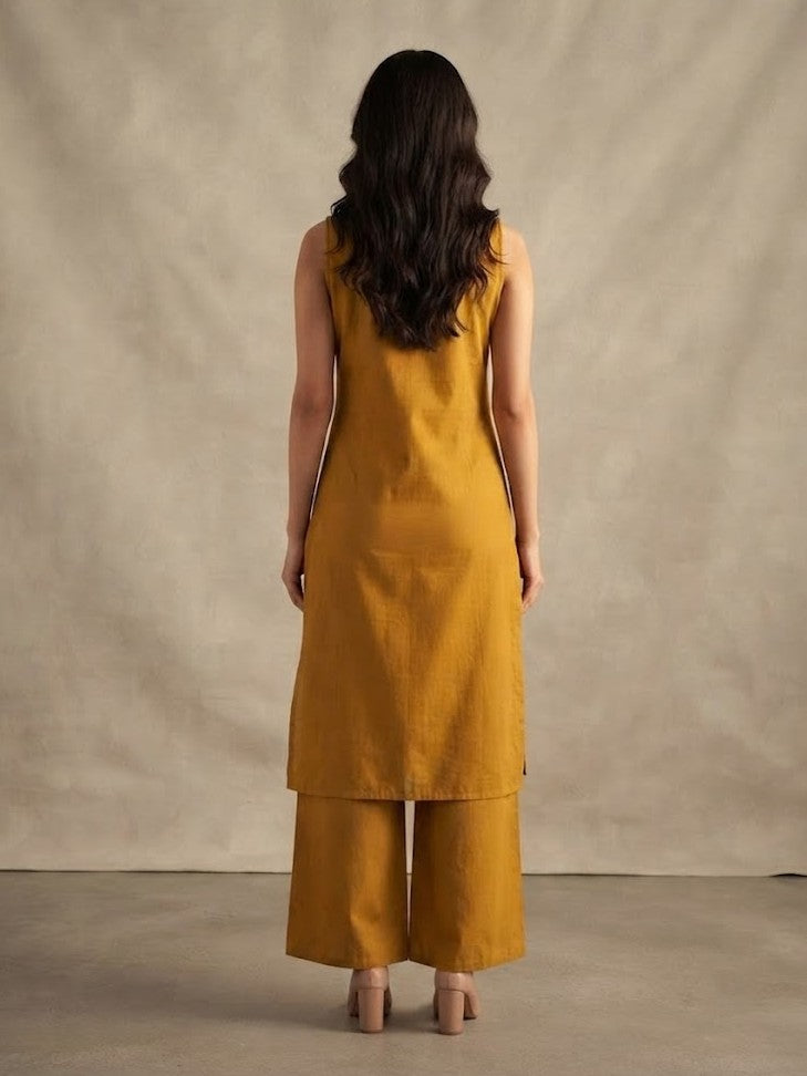 A woman modeling a mustard yellow kurta set with floral embroidery and tassel details, paired with matching wide-leg pants, against a neutral beige backdrop.