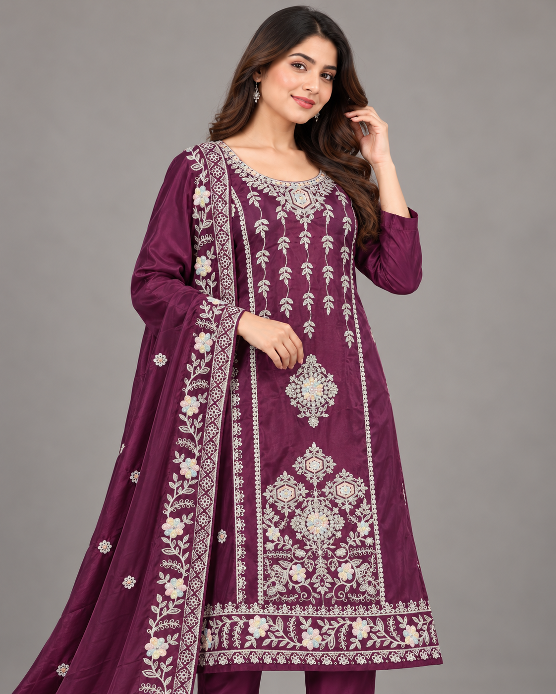 A woman modeling a traditional Indian salwar kameez suit in deep purple with intricate silver and white embroidery, paired with matching pants and a dupatta, set against a plain gray studio background.