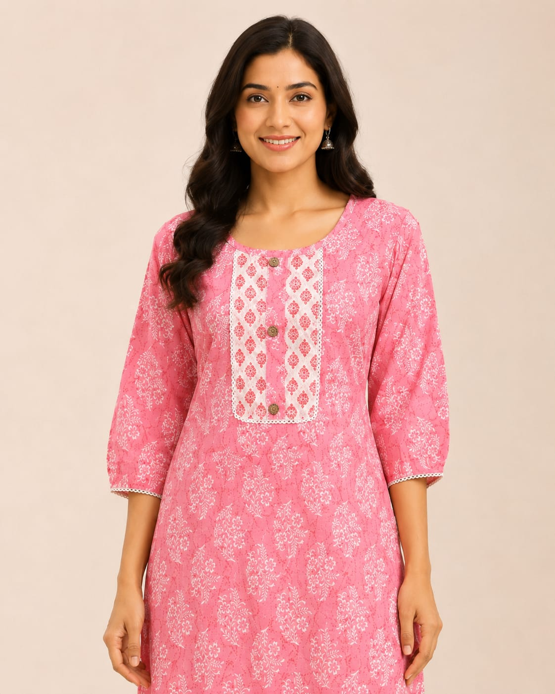 A woman modeling a pink printed kurta with white embroidered detailing on the chest, paired with matching pink and white patterned pants, against a solid light beige background.