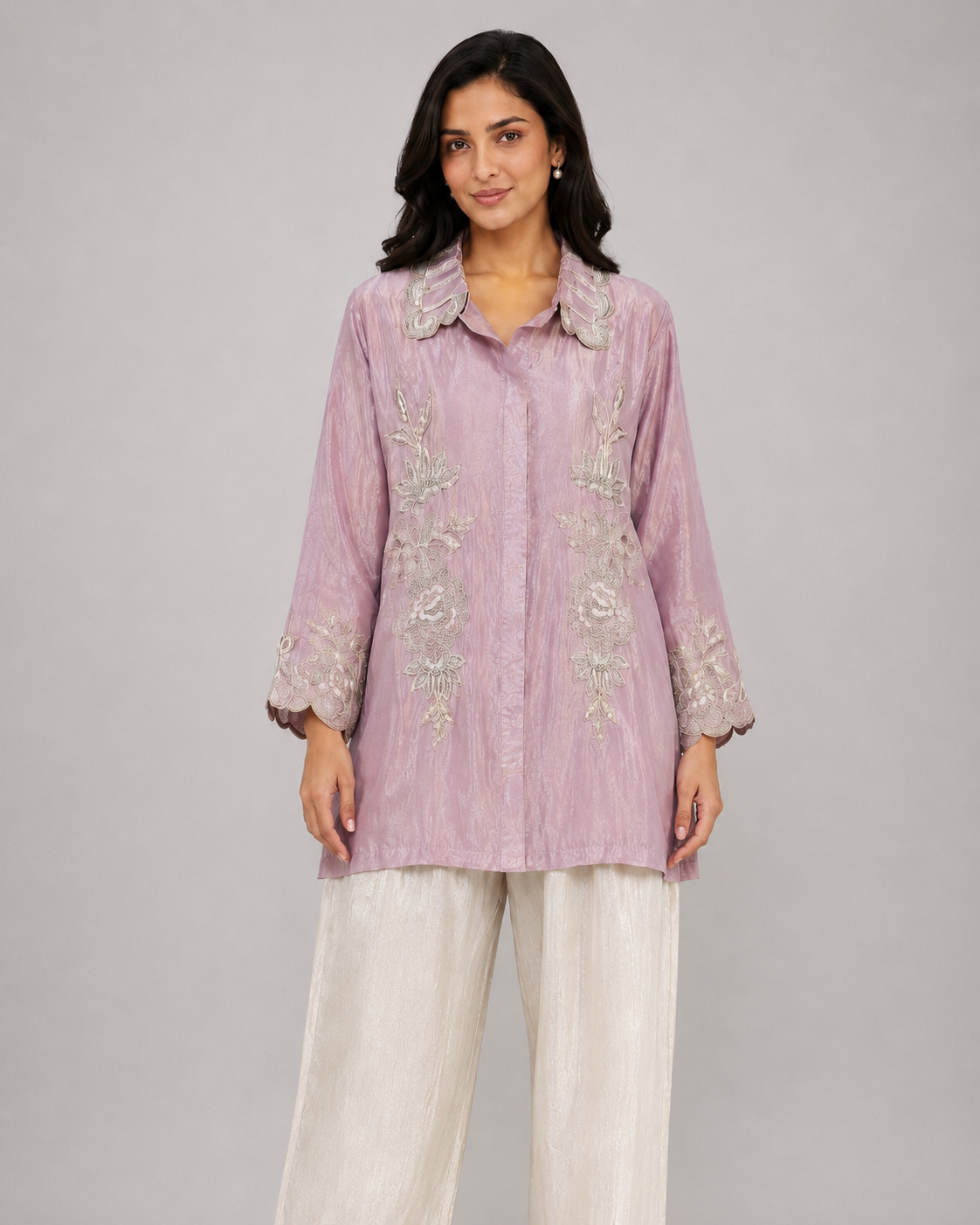 A woman modeling a light pink embroidered kurta paired with white satin palazzo pants and nude heels, set against a solid gray studio background.