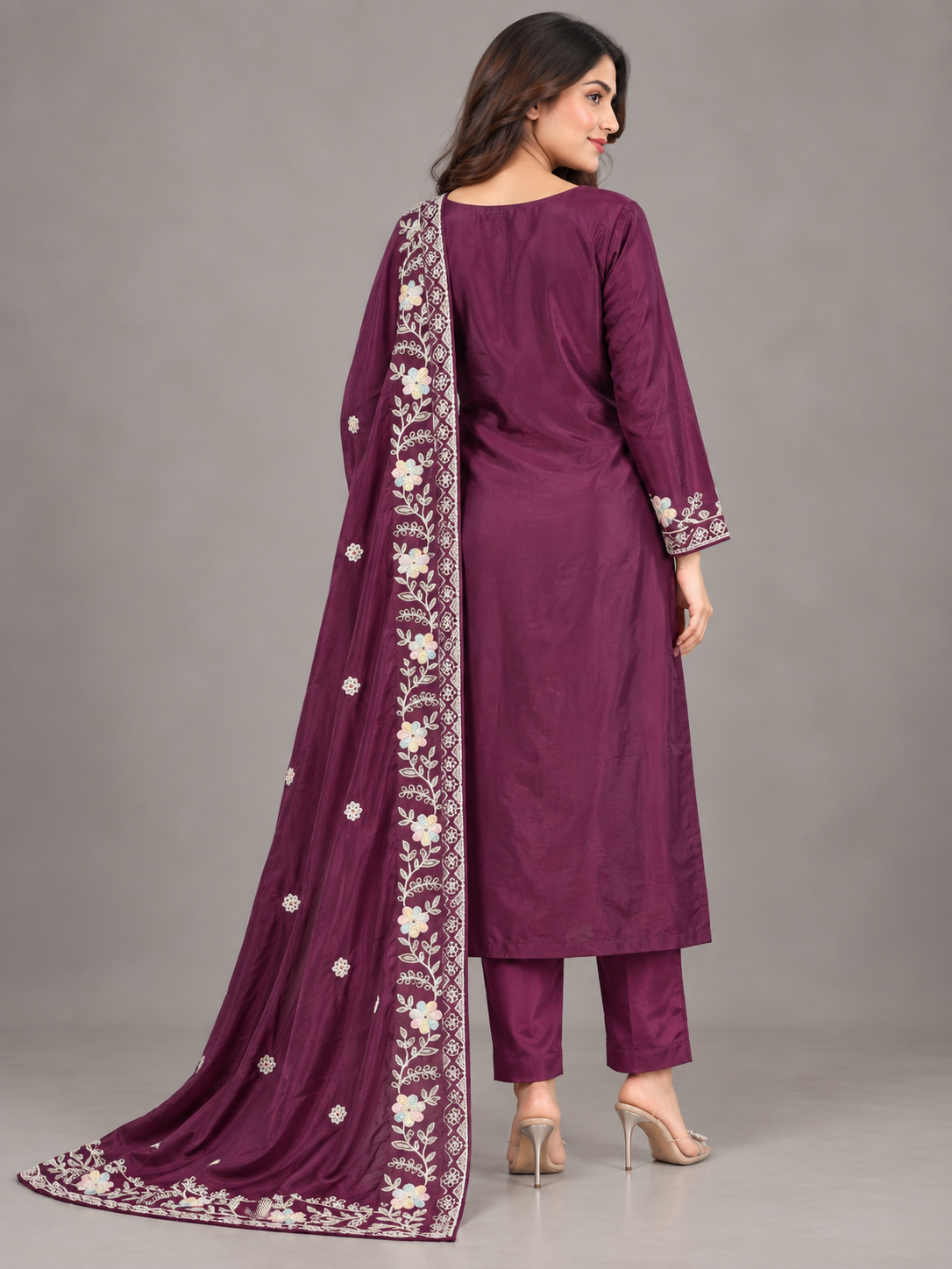 A woman modeling a traditional Indian salwar kameez suit in deep purple with intricate silver and white embroidery, paired with matching pants and a dupatta, set against a plain gray studio background.