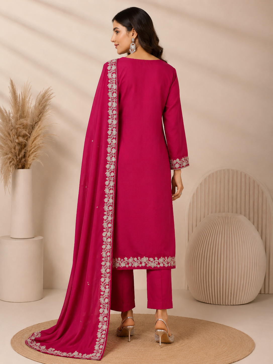 A woman models a magenta pink ethnic salwar kameez suit with silver floral embroidery and a matching dupatta, set against a neutral beige background.