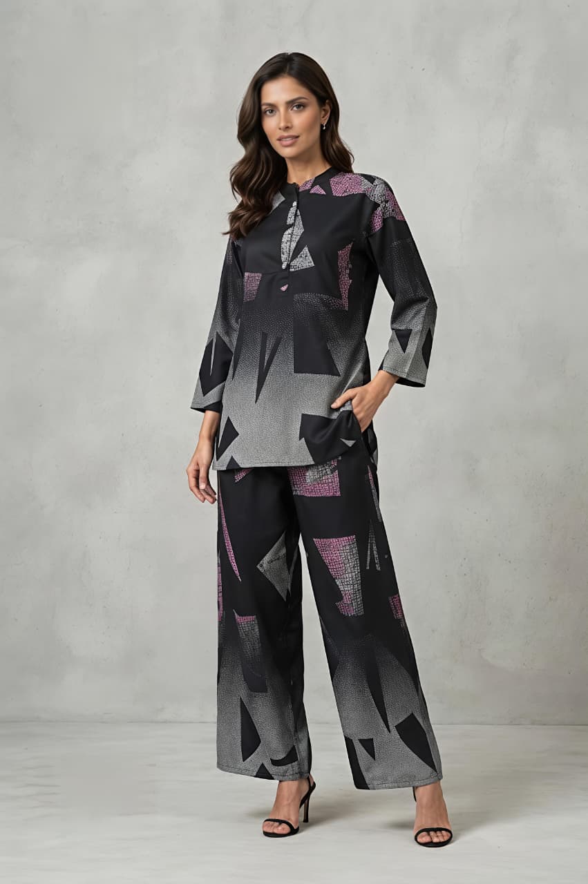 A woman models a matching two-piece set featuring a long-sleeve collared top and wide-leg trousers, both decorated with a modern geometric pattern in shades of gray, black, and pink, set against a textured gray studio backdrop.