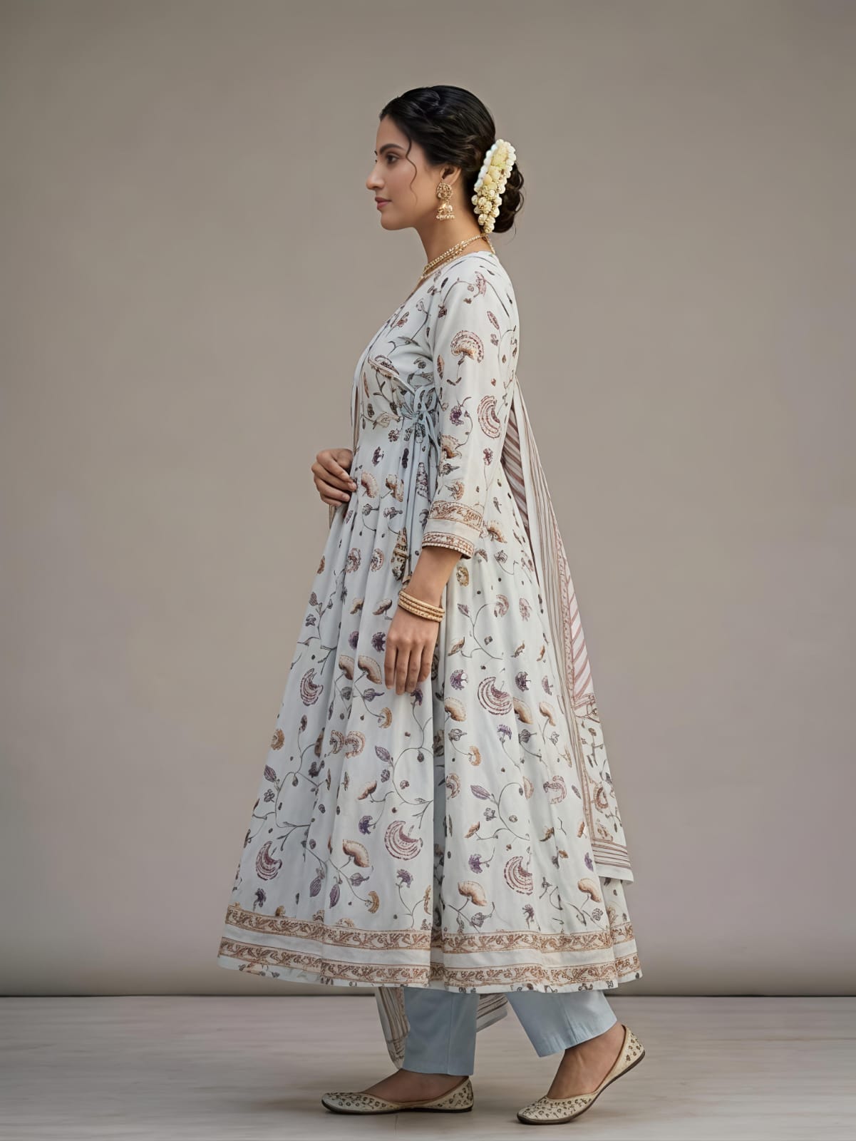 A woman models a traditional Indian outfit consisting of a white printed Anarkali kurta, a matching printed dupatta, and light blue jeans against a neutral studio background.