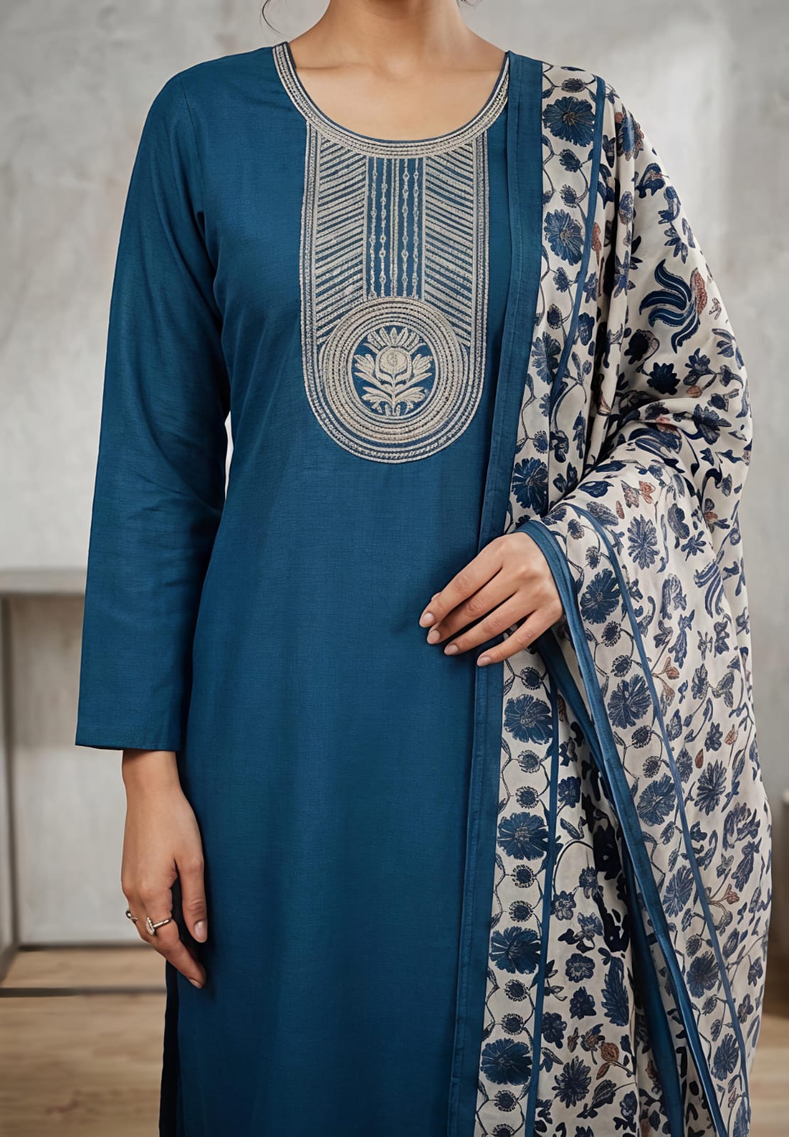 A woman wearing a teal blue kurta with intricate silver embroidery on the chest, paired with a beige and blue floral printed dupatta.