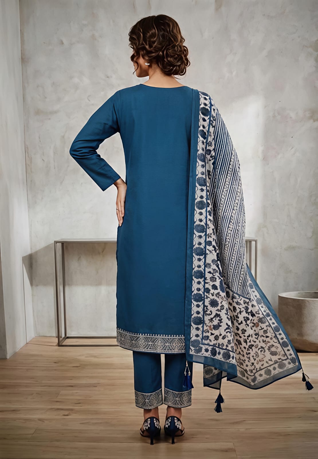 A woman wearing a teal blue kurta with intricate silver embroidery on the chest, paired with a beige and blue floral printed dupatta.