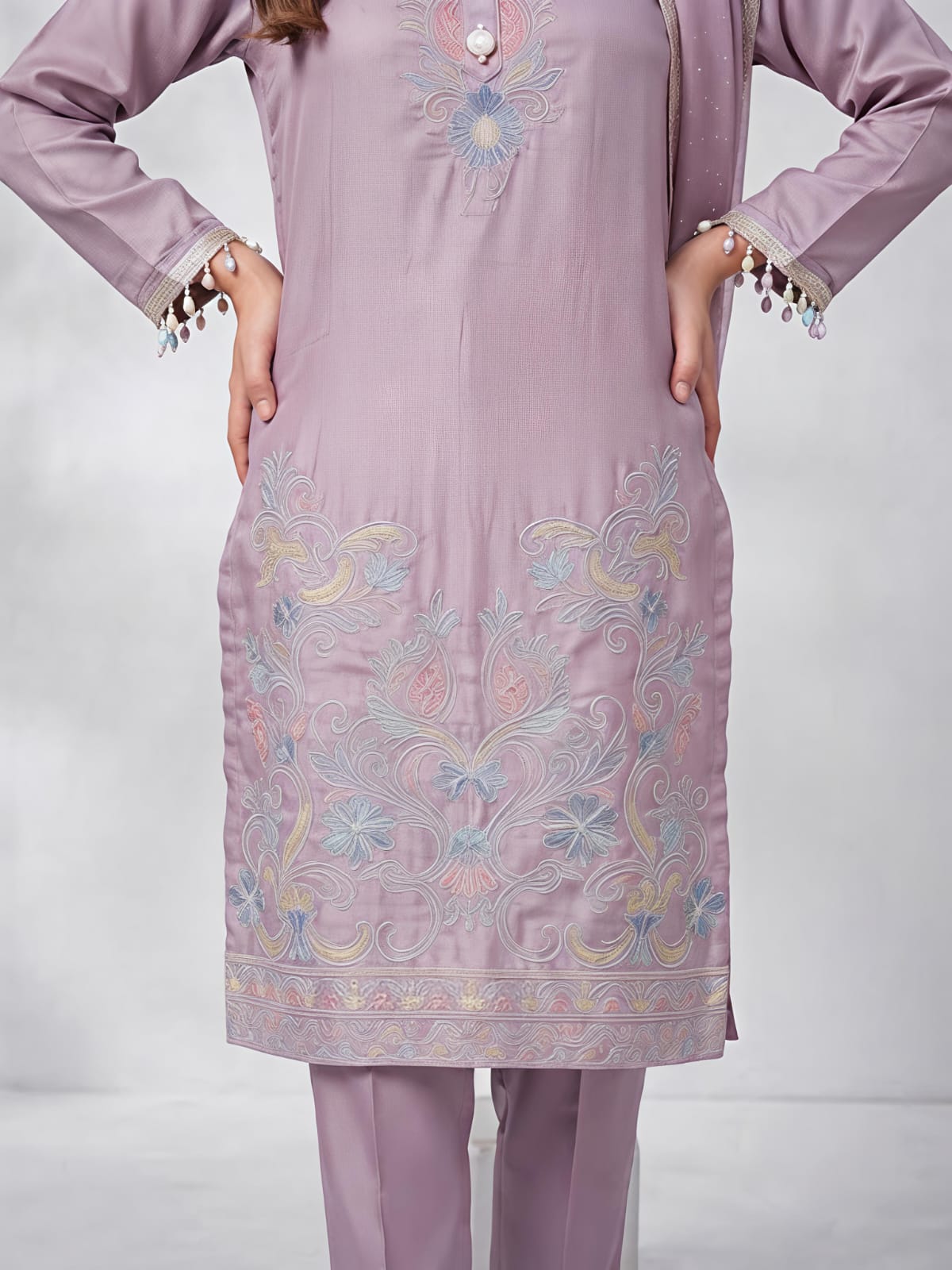 A woman models a three-piece traditional South Asian salwar kameez set in a dusty lavender purple. The set includes a long-sleeved embroidered kameez kurta, matching trousers, and a sheer dupatta.