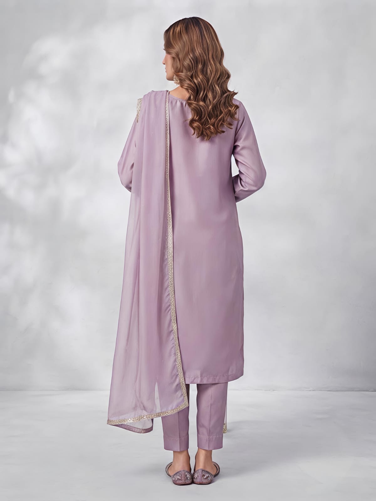 A woman models a three-piece traditional South Asian salwar kameez set in a dusty lavender purple. The set includes a long-sleeved embroidered kameez kurta, matching trousers, and a sheer dupatta.