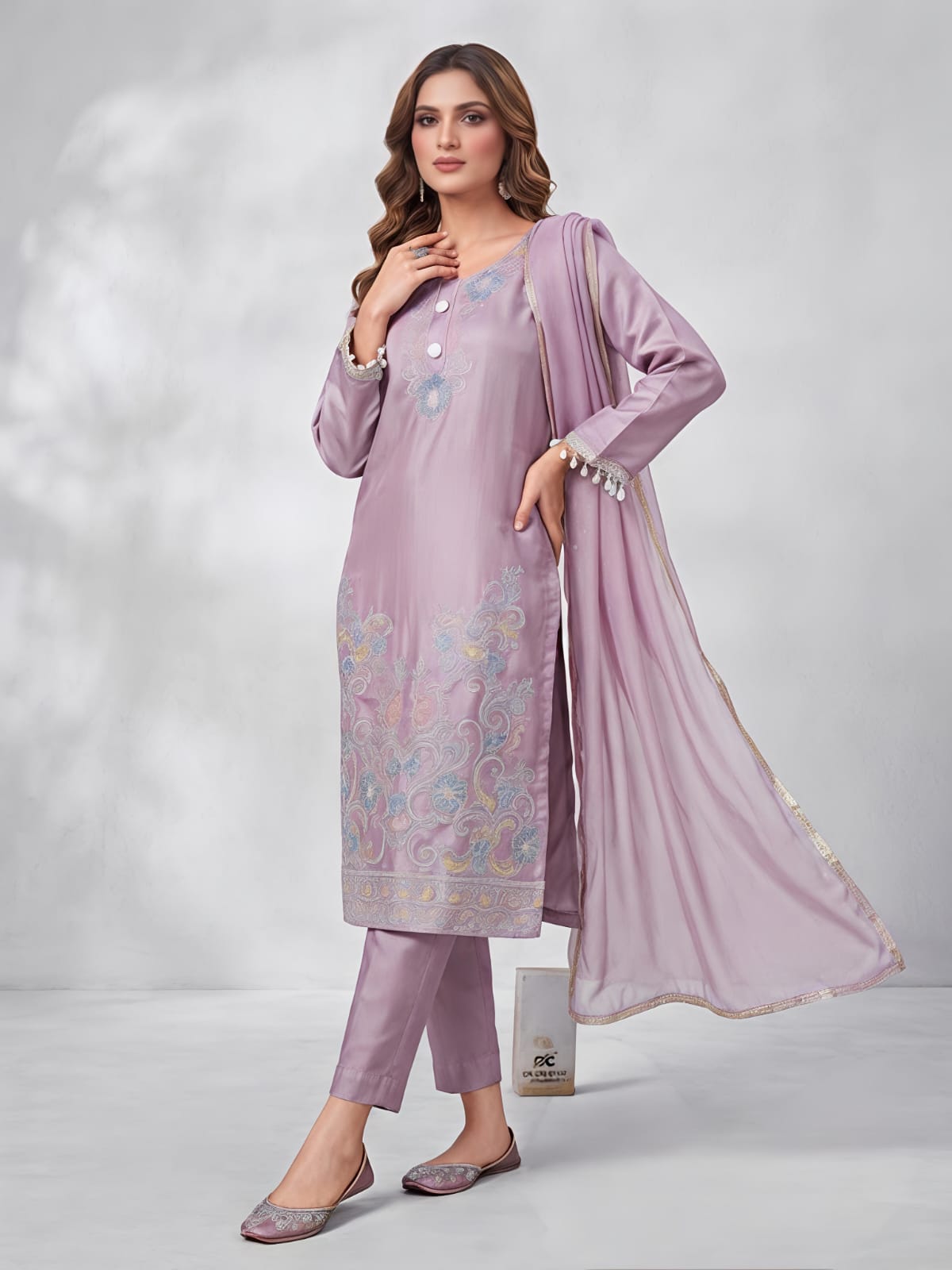 A woman models a three-piece traditional South Asian salwar kameez set in a dusty lavender purple. The set includes a long-sleeved embroidered kameez kurta, matching trousers, and a sheer dupatta.