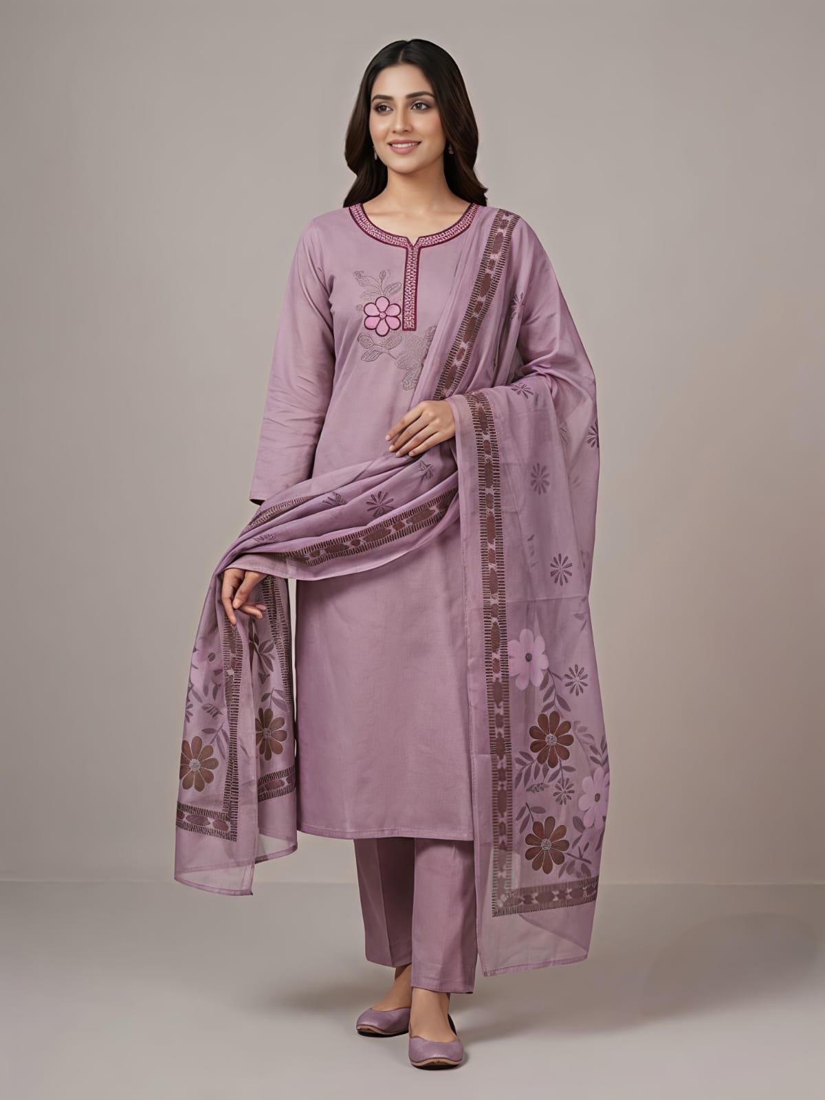 A woman modeling a lavender purple traditional Indian salwar kameez suit with matching pants and a dupatta featuring floral embroidery and border details, set against a plain beige studio background.