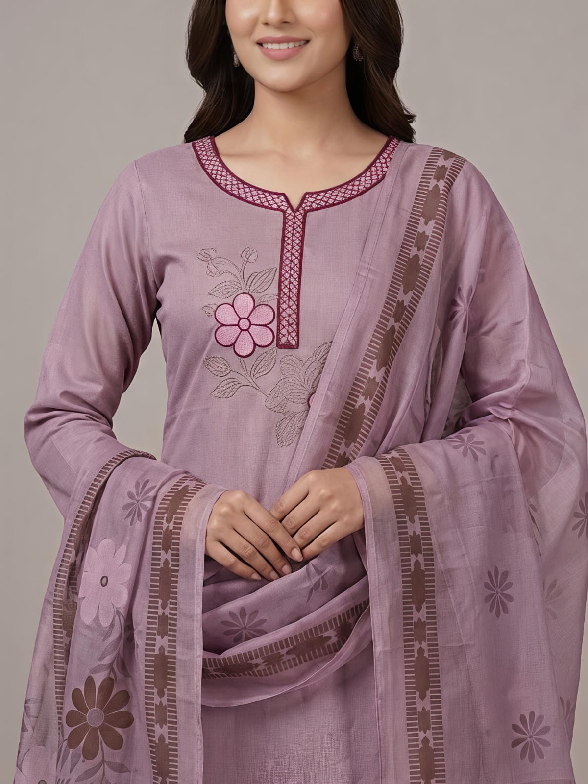 A woman modeling a lavender purple traditional Indian salwar kameez suit with matching pants and a dupatta featuring floral embroidery and border details, set against a plain beige studio background.