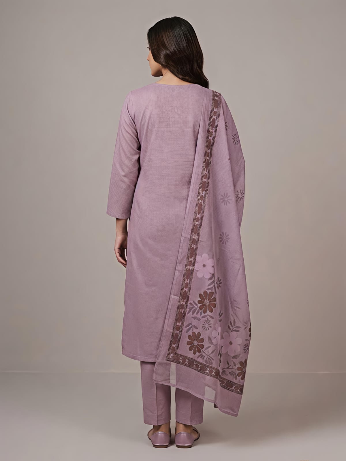 A woman modeling a lavender purple traditional Indian salwar kameez suit with matching pants and a dupatta featuring floral embroidery and border details, set against a plain beige studio background.