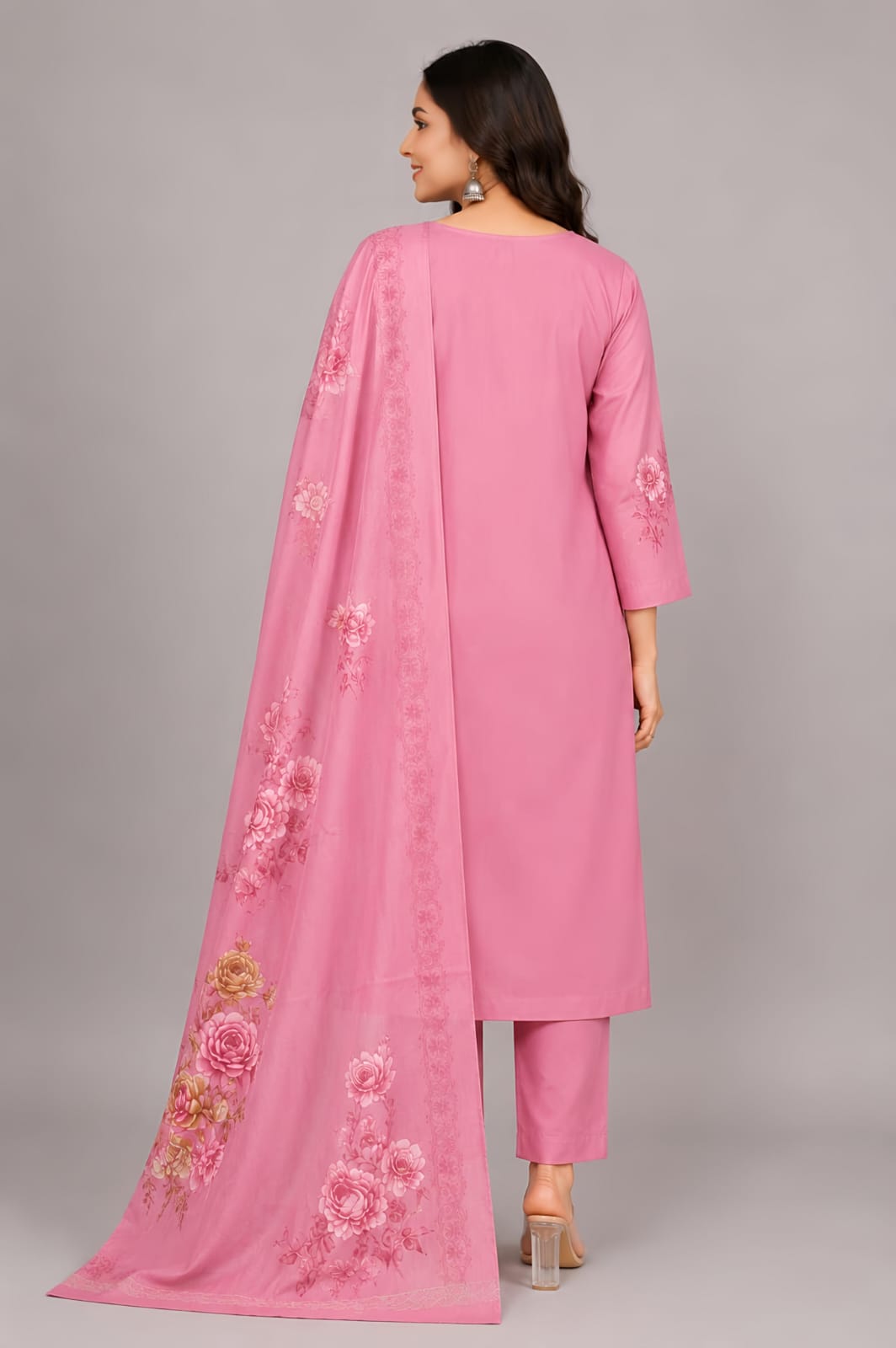 A woman modeling a pink traditional outfit with matching pants and a long sheer dupatta, featuring colorful floral embroidery on the neckline, hem, and dupatta, against a solid gray studio background.