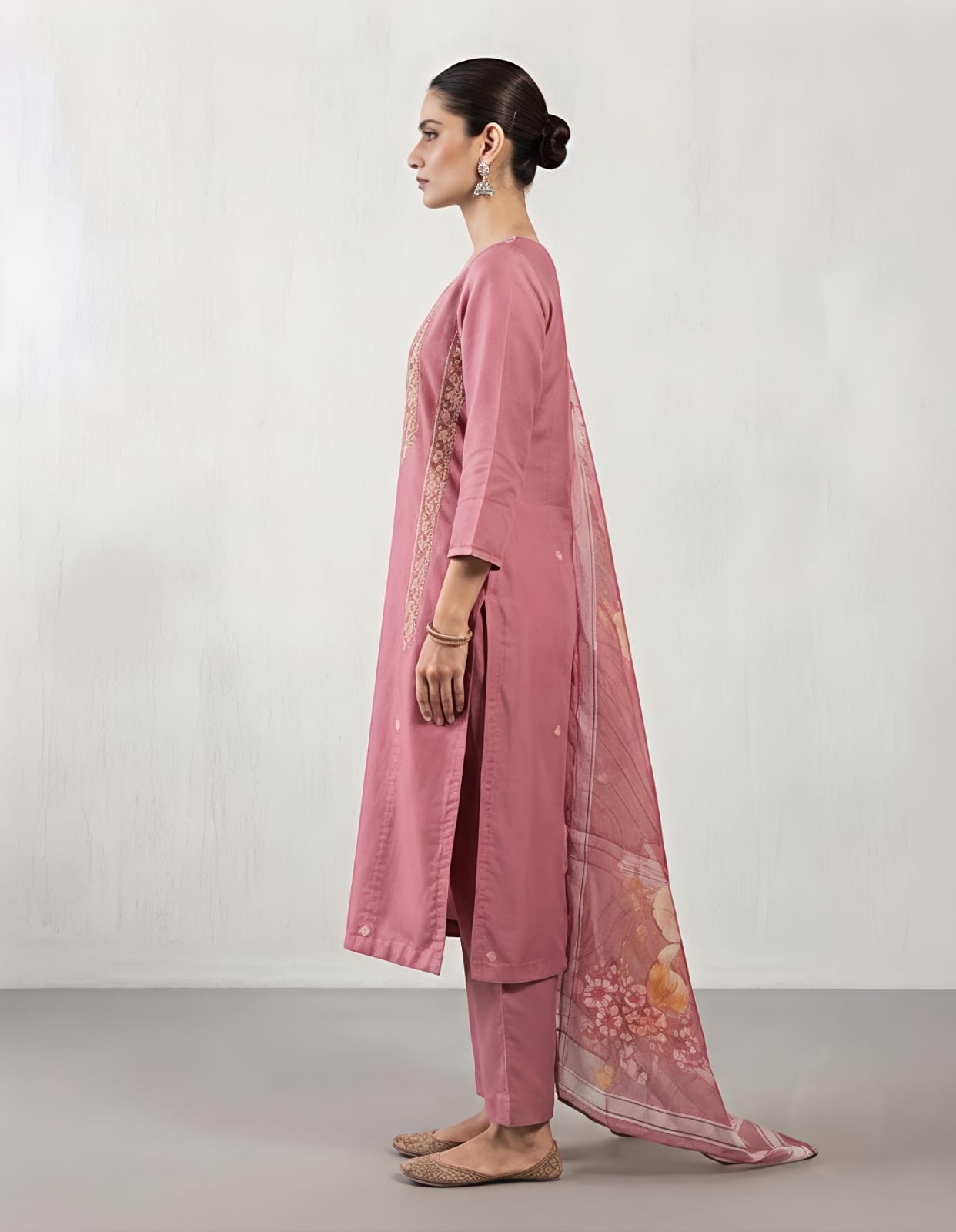 A woman modeling a dusty pink traditional kurta with intricate multicolor embroidery on the chest and a matching sheer floral dupatta, set against a plain light gray background.