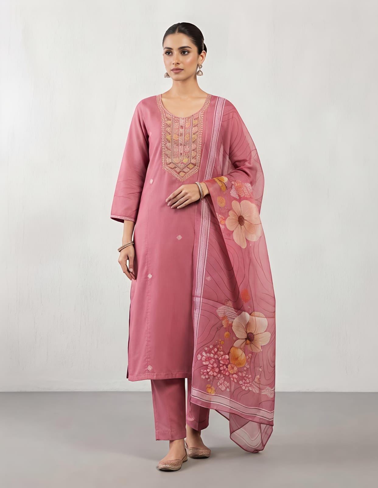 A woman modeling a dusty pink traditional kurta with intricate multicolor embroidery on the chest and a matching sheer floral dupatta, set against a plain light gray background.