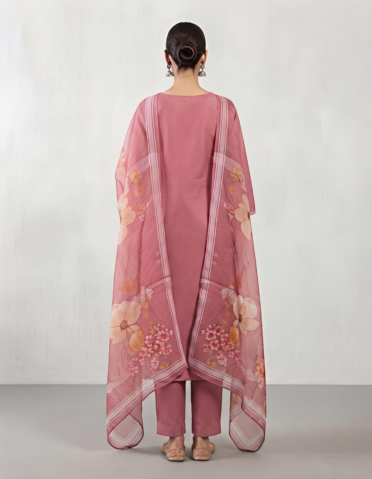 A woman modeling a dusty pink traditional kurta with intricate multicolor embroidery on the chest and a matching sheer floral dupatta, set against a plain light gray background.