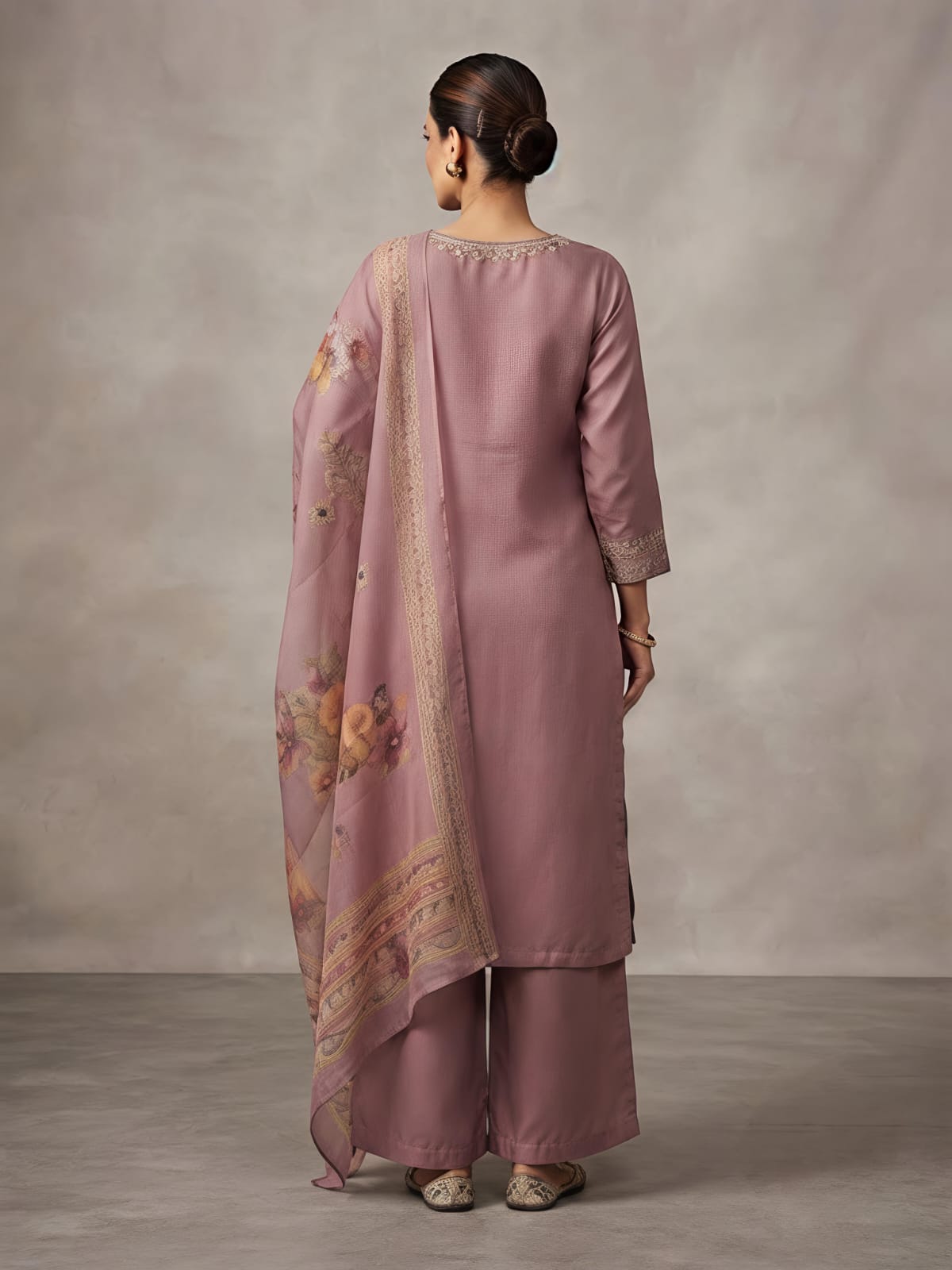 A woman models a dusty pink traditional Indian outfit consisting of a long kurta with floral embroidery, matching wide-leg trousers, and a coordinating dupatta, set against a neutral studio backdrop.