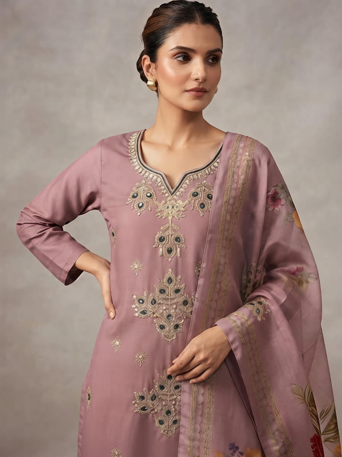 A woman models a dusty pink traditional Indian outfit consisting of a long kurta with floral embroidery, matching wide-leg trousers, and a coordinating dupatta, set against a neutral studio backdrop.