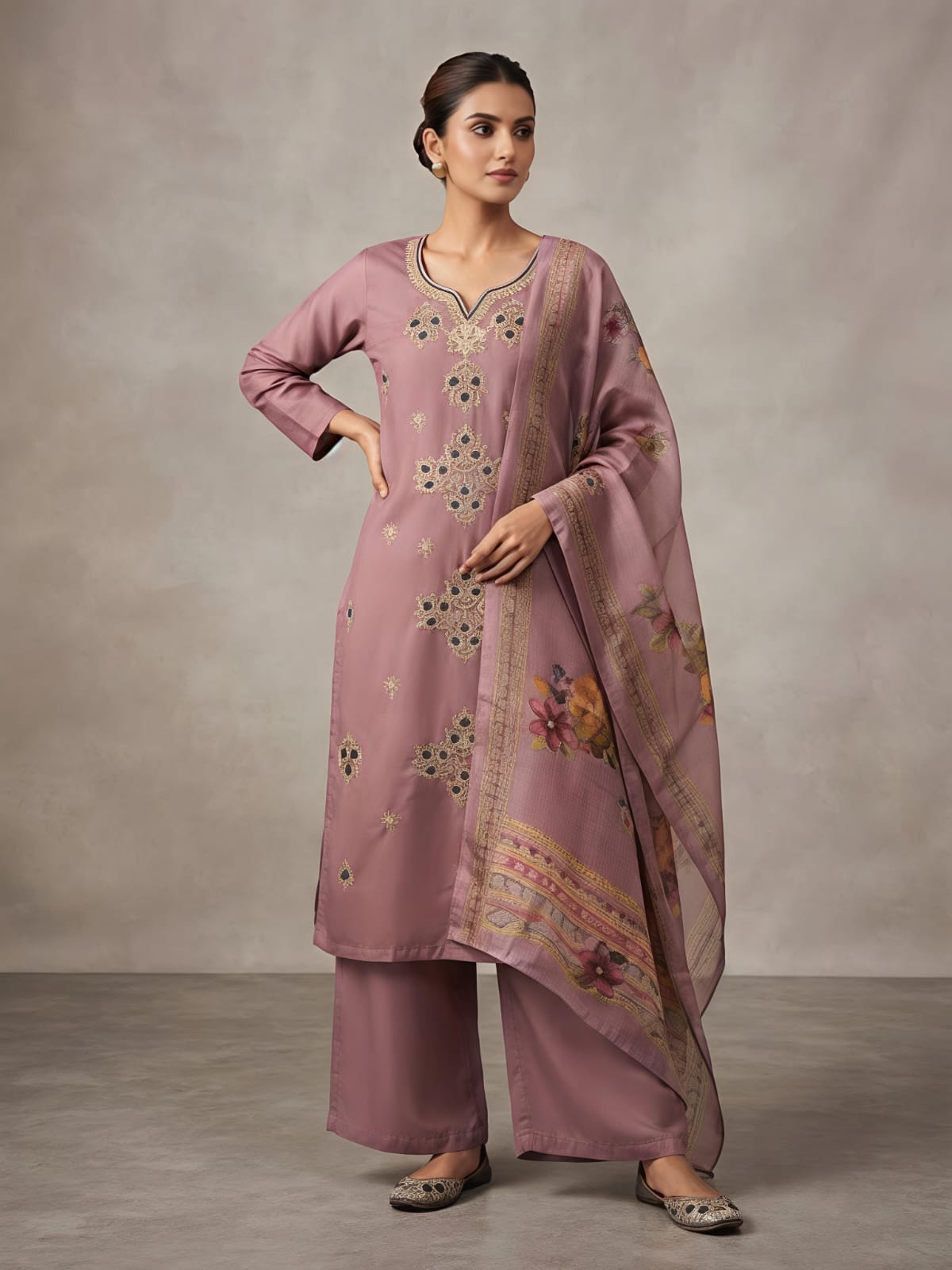 A woman models a dusty pink traditional Indian outfit consisting of a long kurta with floral embroidery, matching wide-leg trousers, and a coordinating dupatta, set against a neutral studio backdrop.