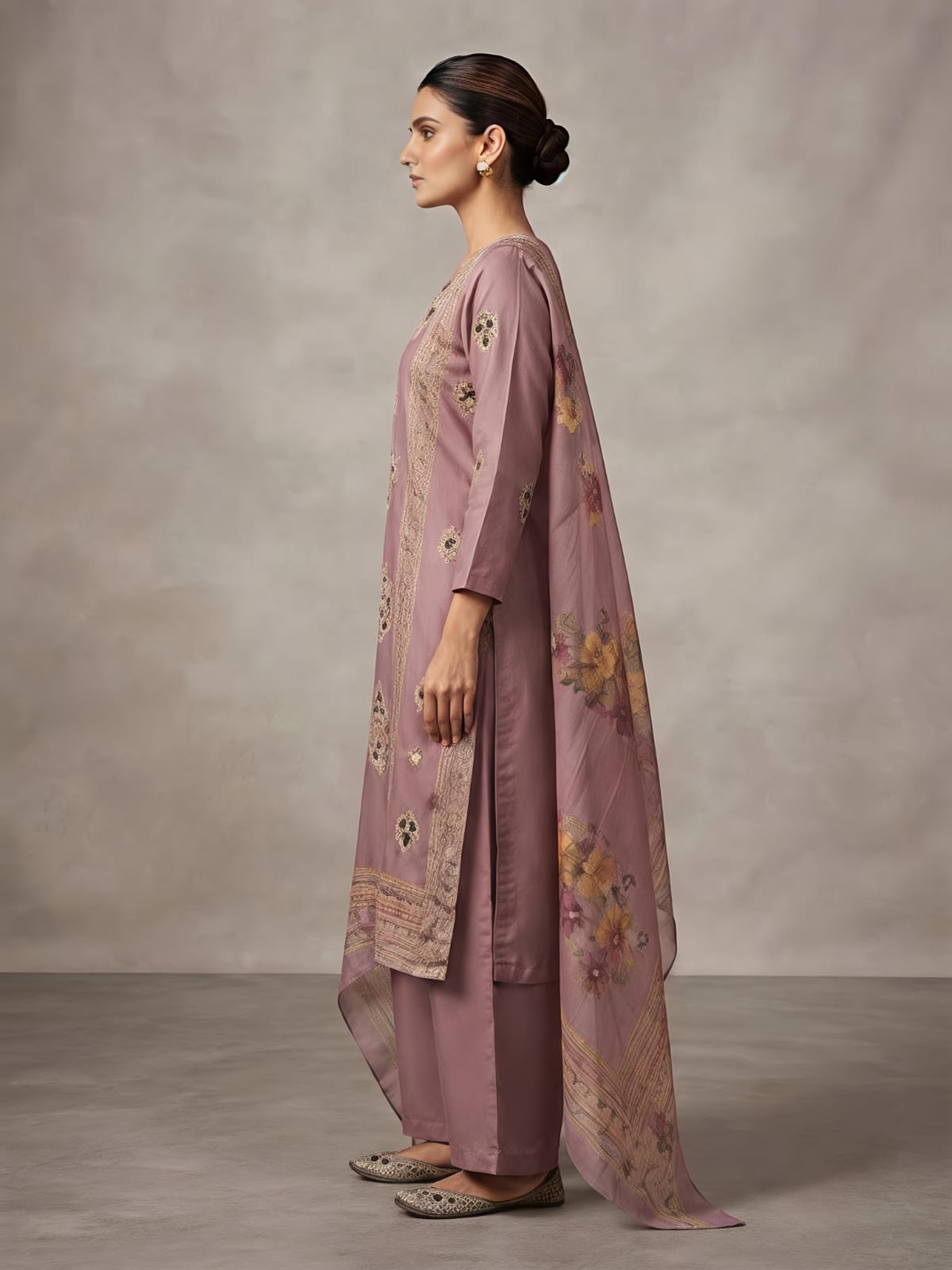 A woman models a dusty pink traditional Indian outfit consisting of a long kurta with floral embroidery, matching wide-leg trousers, and a coordinating dupatta, set against a neutral studio backdrop.