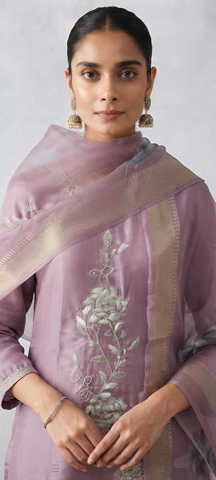 A woman models a lavender purple three-piece traditional outfit consisting of a kurta with floral embroidery, matching trousers, and a sheer dupatta draped over her shoulder, set against a neutral studio background.