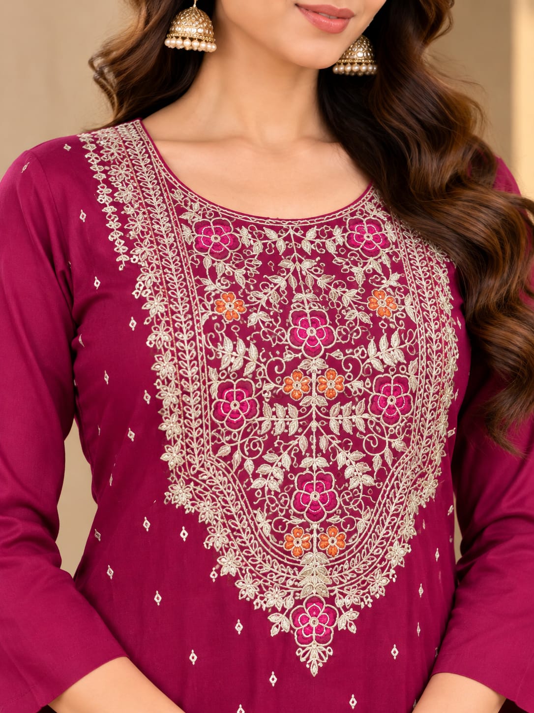 A woman models a traditional Indian salwar kameez suit in a rich magenta-purple color. The set includes a kurta with detailed silver and gold embroidery around the neckline, matching trousers, and a sheer dupatta decorated with silver circular motifs and borders.