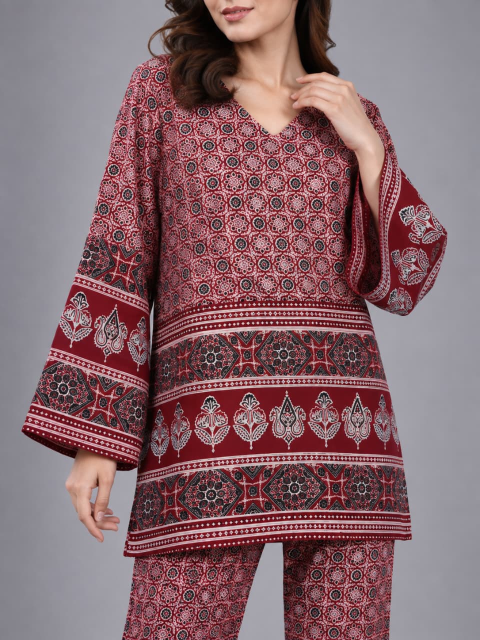 A woman modeling a matching two-piece kurta and trouser set with a red, pink, and black floral block print pattern, set against a solid gray studio background.
