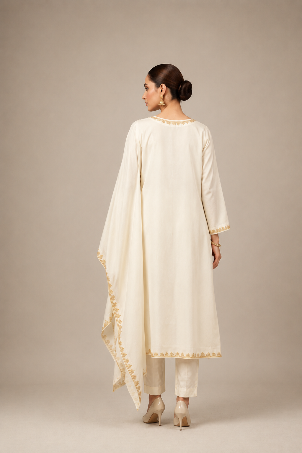A woman modeling a traditional cream-colored Indian outfit consisting of a long kurta with gold embroidery, matching trousers, and a draped dupatta, set against a plain beige studio background.