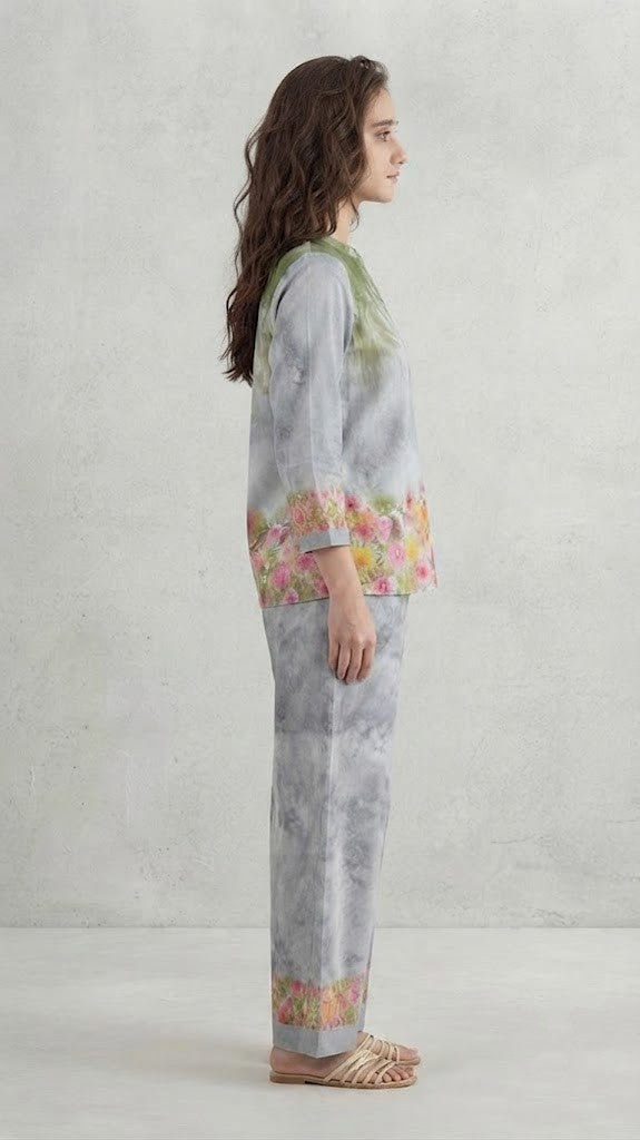 A woman modeling a two-piece traditional outfit featuring a light gray and white tie-dye kurta with green embroidery and colorful floral prints, paired with matching wide-leg trousers.