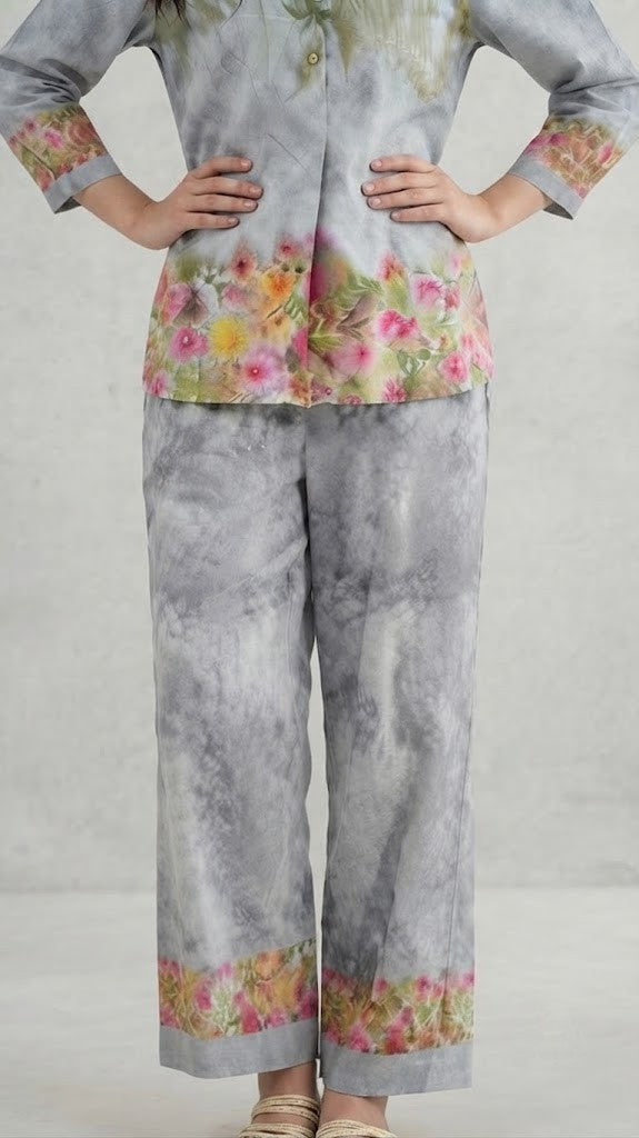 A woman modeling a two-piece traditional outfit featuring a light gray and white tie-dye kurta with green embroidery and colorful floral prints, paired with matching wide-leg trousers.