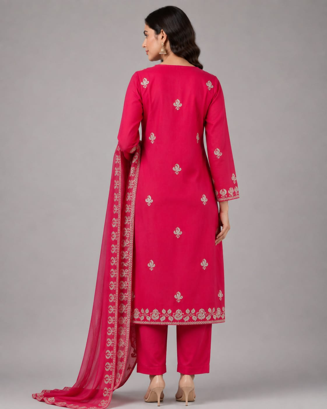 A woman modeling a bright pink traditional Indian outfit with a matching sheer dupatta, featuring intricate white floral embroidery on the kurta and dupatta, paired with matching pink trousers, against a neutral gray studio background.