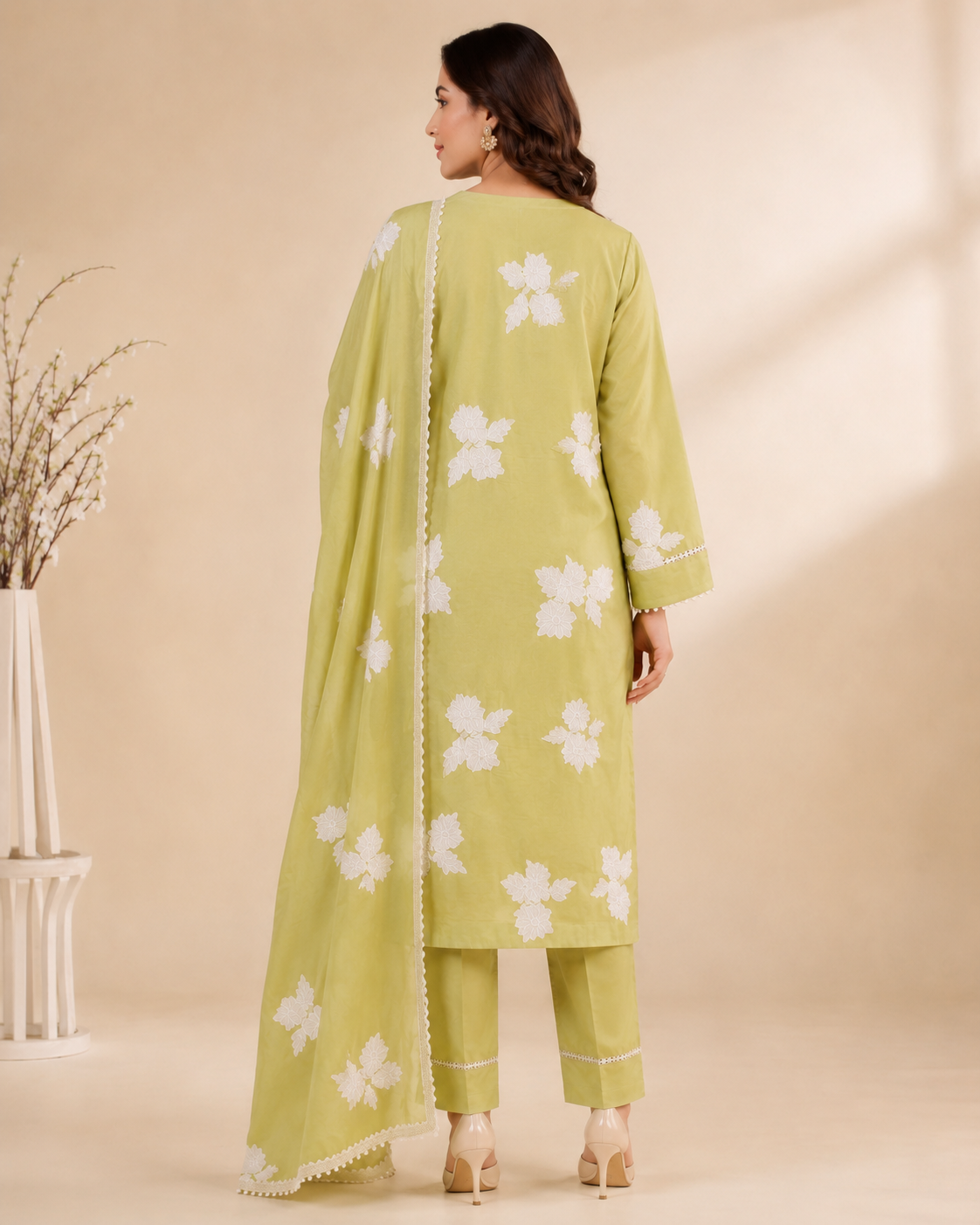 A woman models a light Yellow three-piece salwar kameez suit with white floral embroidery, matching trousers, and a coordinating dupatta, set against a warm beige background.