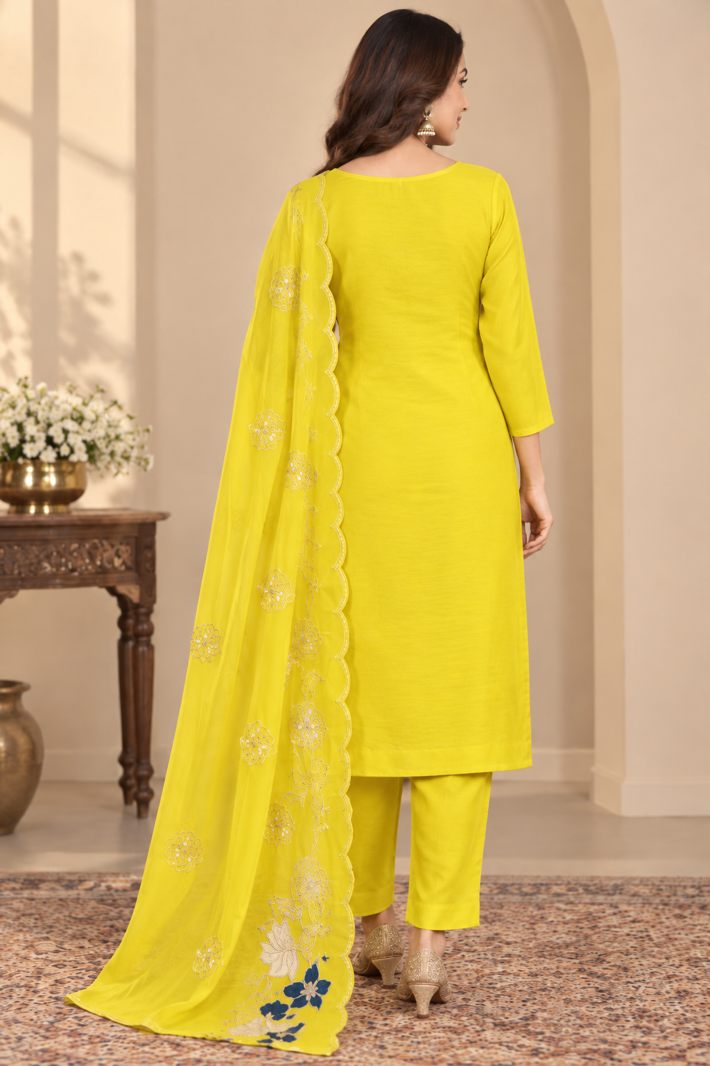 A woman models a bright yellow Indian ethnic salwar kameez suit with blue and white floral embroidery, featuring a matching dupatta, in an indoor setting.